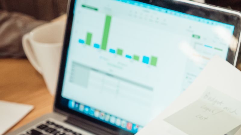 A modern workspace showing hands analyzing marketing data on a laptop and paper documents.